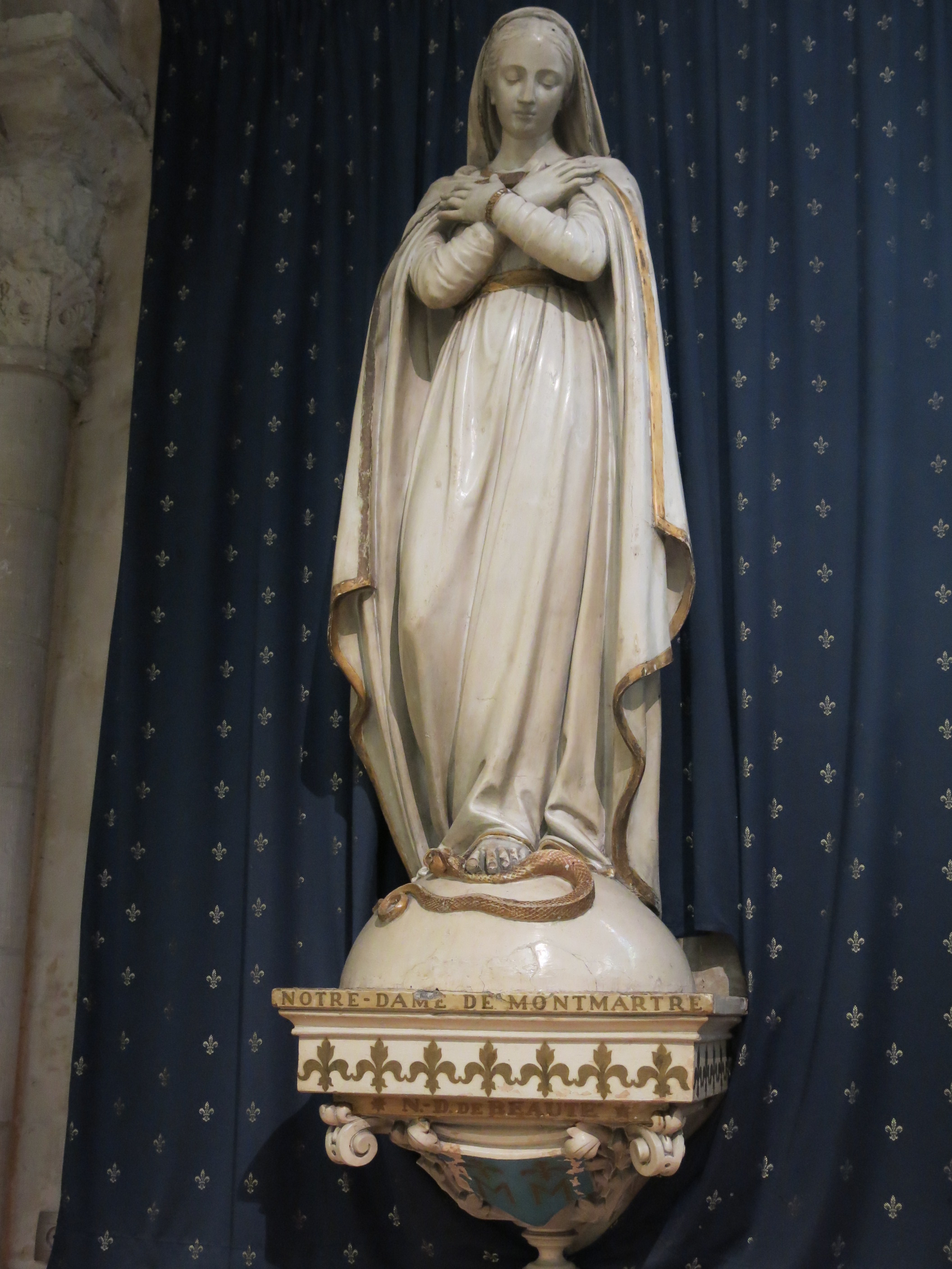 Statue de Notre-Dame de Beauté, sainte patronne de la paroisse Saint-Pierre de Montmartre, devant une tenture bleue fleurdelisée.